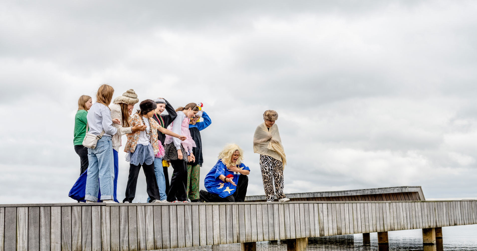 Foto: Mette Johnsen. Motiv: Børn og kunstner i kostumer står på bro ved fjorden Nykøbing.